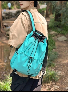 Cyan nylon drawstring backpack with KEMIBAG logo shown in a forest stream setting