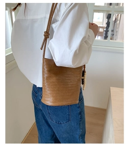 Detail of a brown woven bucket bag with long shoulder strap and vintage wooden bead charm