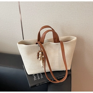 Detail of beige canvas tote bag featuring brown leather straps and wooden bead charm accessory