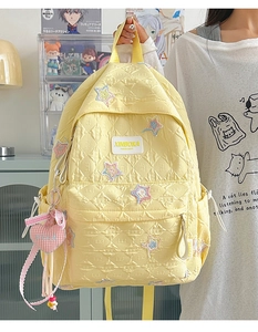 Detail of light yellow quilted backpack with colorful star patches and heart charm