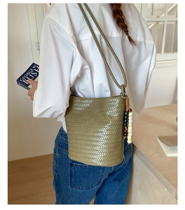 Olive green woven bucket bag with beaded tassels styled on a model in a white shirt