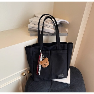 Close-up of black canvas tote bag with dual front pockets and a cute bear charm accessory