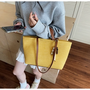 Detailed view of yellow canvas tote bag featuring brown leather handles and beaded charm