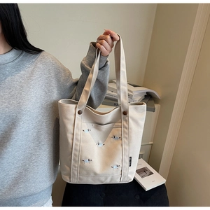 Détail d'un grand sac cabas en toile beige avec broderie de chien bleu et étiquette