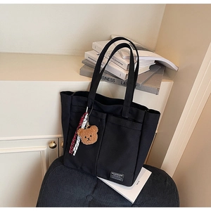 Detail of black canvas tote bag featuring large front pockets and a brown bear charm
