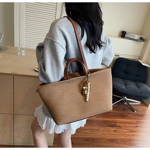 Detail of a brown canvas tote bag with leather handles and decorative wooden beads