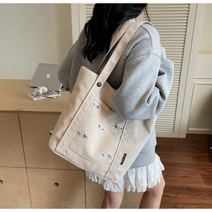 Détail d'un cabas en toile beige avec broderie de chien et étiquette de marque