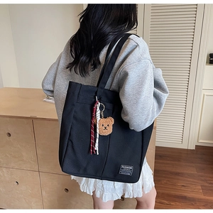 Detail view of black canvas tote bag with fashion label and brown bear pendant
