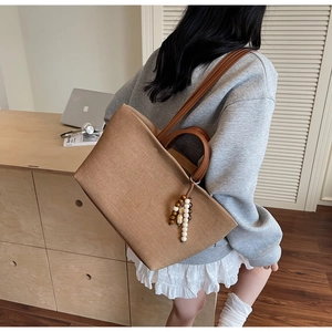 Detail of a brown canvas tote bag with wooden bead pendant and faux leather handles