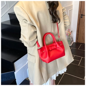 Dettaglio di una borsa a secchiello rossa con fiocco indossata su un blazer beige