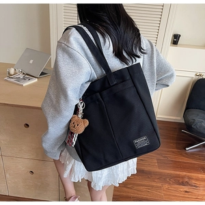 Detail of black canvas tote bag with fashion tag and brown plush bear charm accessory