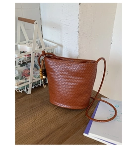 Detail of brown woven bucket bag with elegant wooden bead tassel and smooth leather texture