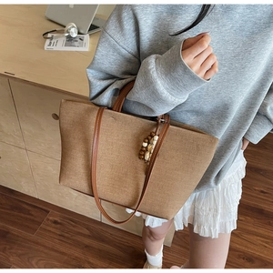 Close-up of a brown canvas tote bag with dual leather handles and wooden bead pendant