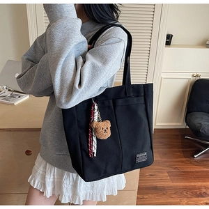 Detail of black canvas tote bag with fashion label, teddy bear charm and striped scarf