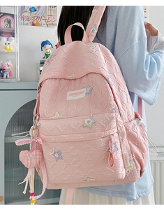 Close-up of pink quilted backpack with rainbow star embroidery and heart charm detail