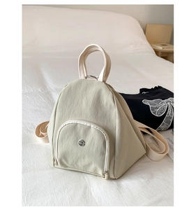 Detail view of the beige nylon backpack featuring front zipper pocket and metal logo plaque