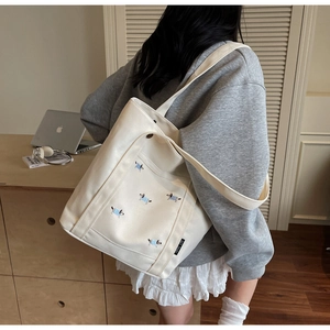 Détail d'un sac cabas en toile crème avec broderies de chiens colorés et étiquette