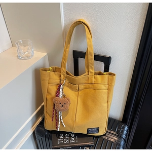 Detail of yellow canvas tote bag with large front pockets and bear plush accessory