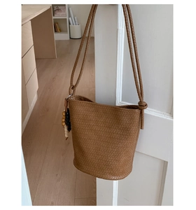 Detail of woven brown bucket bag with rustic wooden bead charm on its side