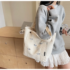 Détail d'un sac cabas en toile avec broderie chiot et étiquette tissée noire sur l'épaule