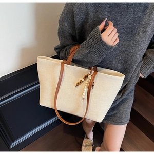 Detail of canvas tote bag with brown leather handles and wooden bead charm on stairs