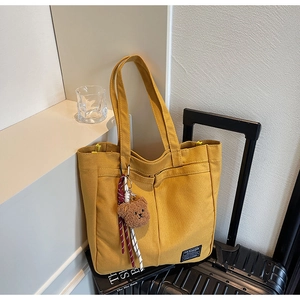 Detail of yellow canvas tote bag with brown bear charm and fashion textile label