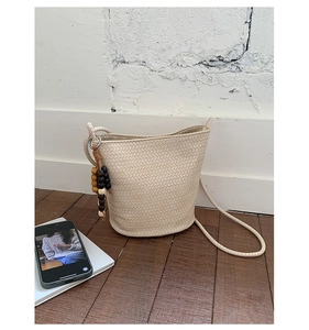 Detail shot of a beige woven bucket bag with wood bead tassel on a wooden floor