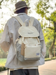 Sac à dos minimaliste en nylon crème avec fermeture à rabat exposé dans un parc
