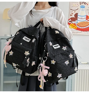 Detailed close-up of a black quilted backpack with embroidered stars and heart charm