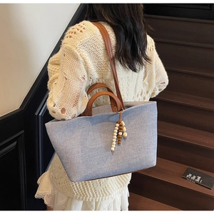 Detail of light blue denim tote bag with brown leather handles and bead charm detail