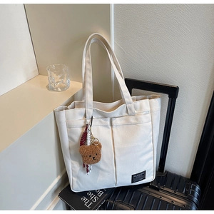 Detail of white canvas tote bag with front pockets and brown plush bear charm