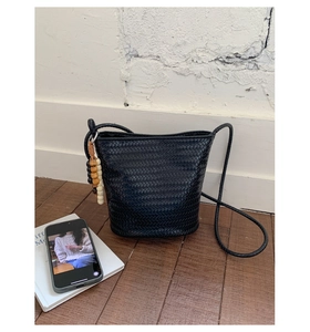 Detail of black woven bucket bag with wooden bead tassels and crossbody strap on wood floor