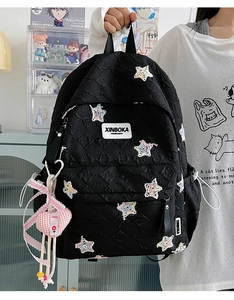 Detail of black quilted backpack with star patches and cute pink heart charm accessory