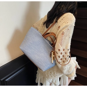 Lifestyle view of large light blue canvas tote bag with brown leather handles and bead tassels