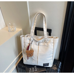 Detail of off-white canvas tote bag with front pockets and cute brown plush bear pendant