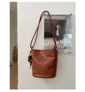 Detail of a brown woven bucket bag featuring decorative wooden beads and a thin leather strap