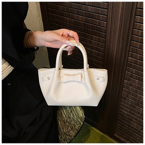 Dettaglio della borsa a secchiello in pelle crema con texture litchi e fiocco decorativo