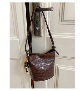 Detail of dark brown woven bucket bag with unique wooden bead charm and slim strap