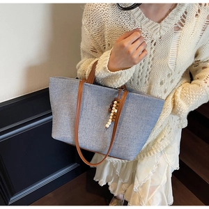 Detail view of large canvas tote bag with brown leather handles and beaded tassel accessory