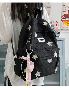 Close-up of a black quilted backpack with star embroidery and a heart charm accessory