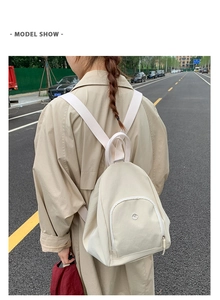 Outdoor model show of a creamy white canvas backpack with circular silver metal logo