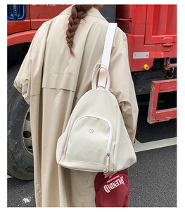 Outdoor shot of cream-white multifunctional backpack featuring metal logo and front pocket