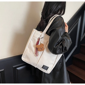 Detail of off-white canvas tote bag with side pocket and cute brown bear pendant