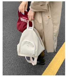 Detail of minimalist beige canvas backpack featuring circular metal logo and front zip pocket