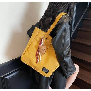 Detail view of large yellow canvas tote bag featuring a cute plush bear charm and striped straps