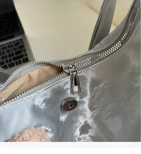 Close-up of smooth metal zipper and magnetic closure on a silver-grey satin tote bag