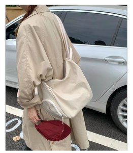 Outdoor view of a beige canvas crossbody bag with white adjustable strap and silver zipper