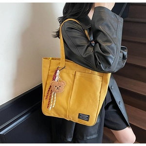 Detail of yellow canvas tote bag featuring external pockets and brown plush bear charm