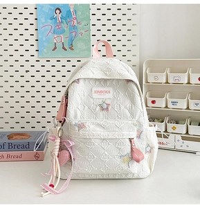 Close-up of white quilted star backpack with pink heart charm in a school setting