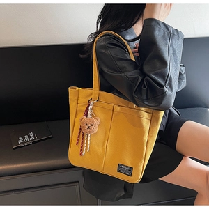 Close-up of bright yellow canvas tote bag with fashion label and bear pendant details